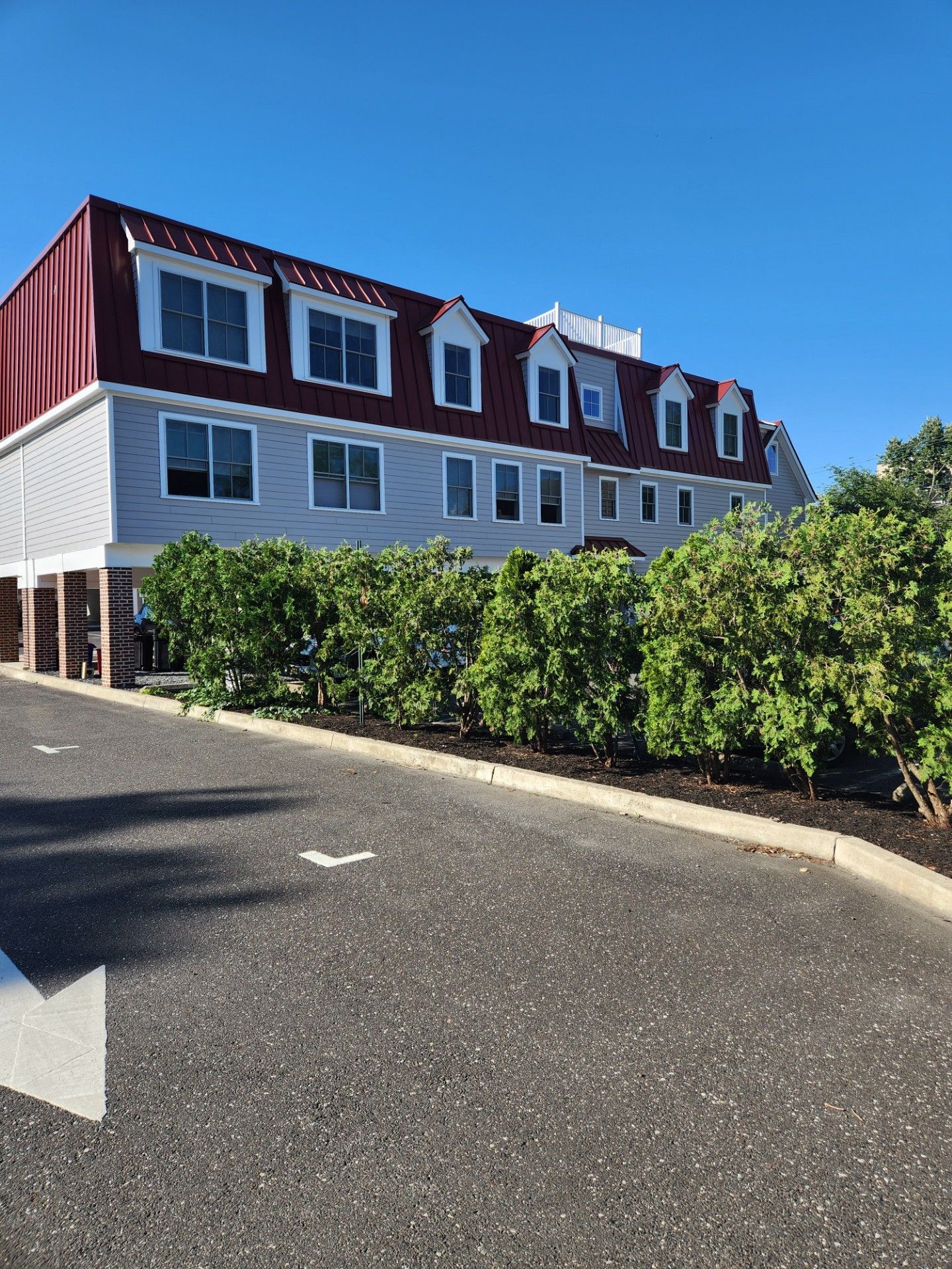 A large white building with a red roof is surrounded by trees and bushes.