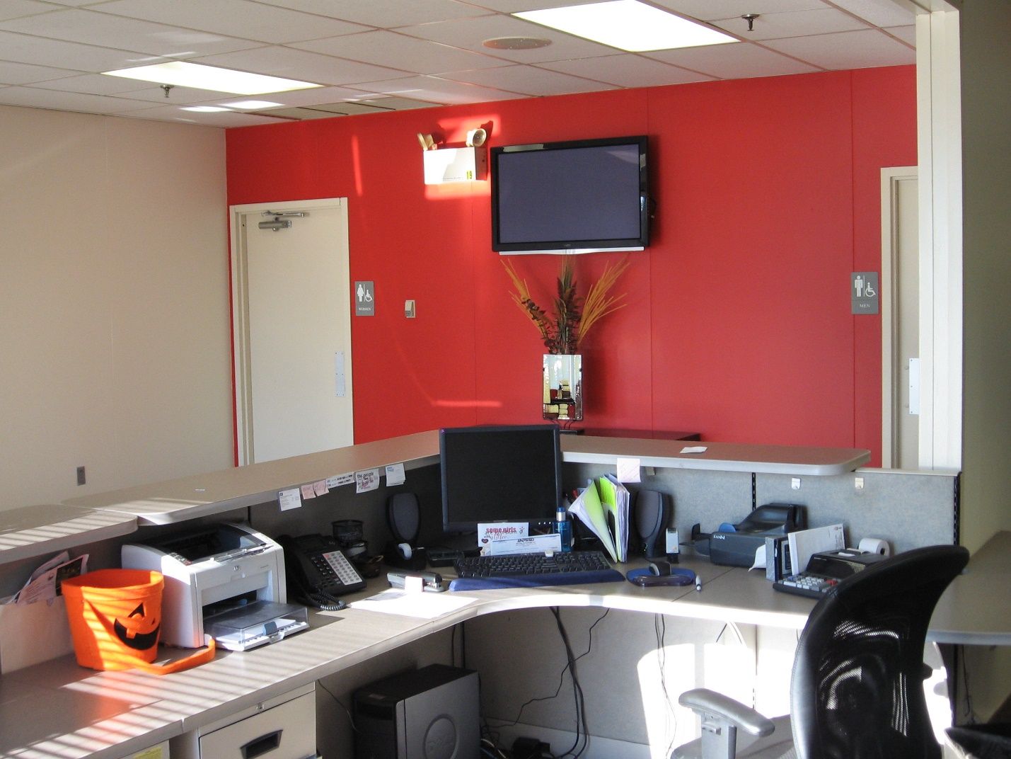 A cubicle with a computer and a TV on the wall.