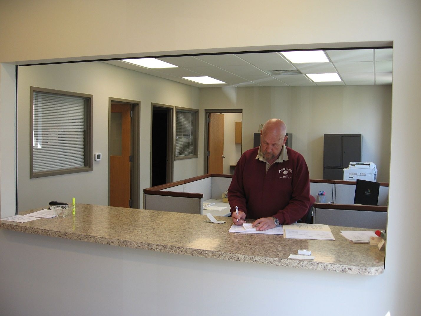 A man in a maroon shirt is sitting at a counter in an office.