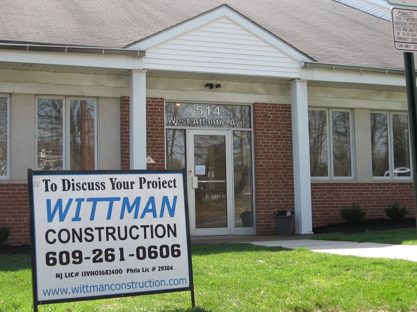 A sign for wittman construction is in front of a brick building.