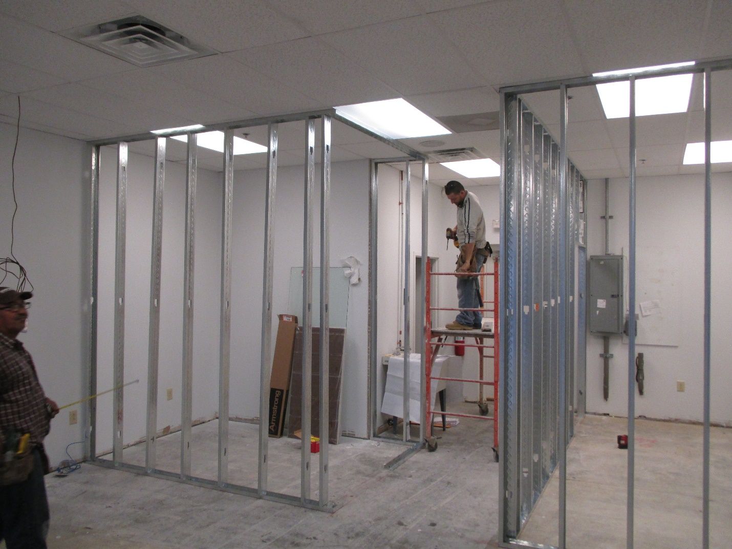 A man is standing on a ladder in a room under construction.