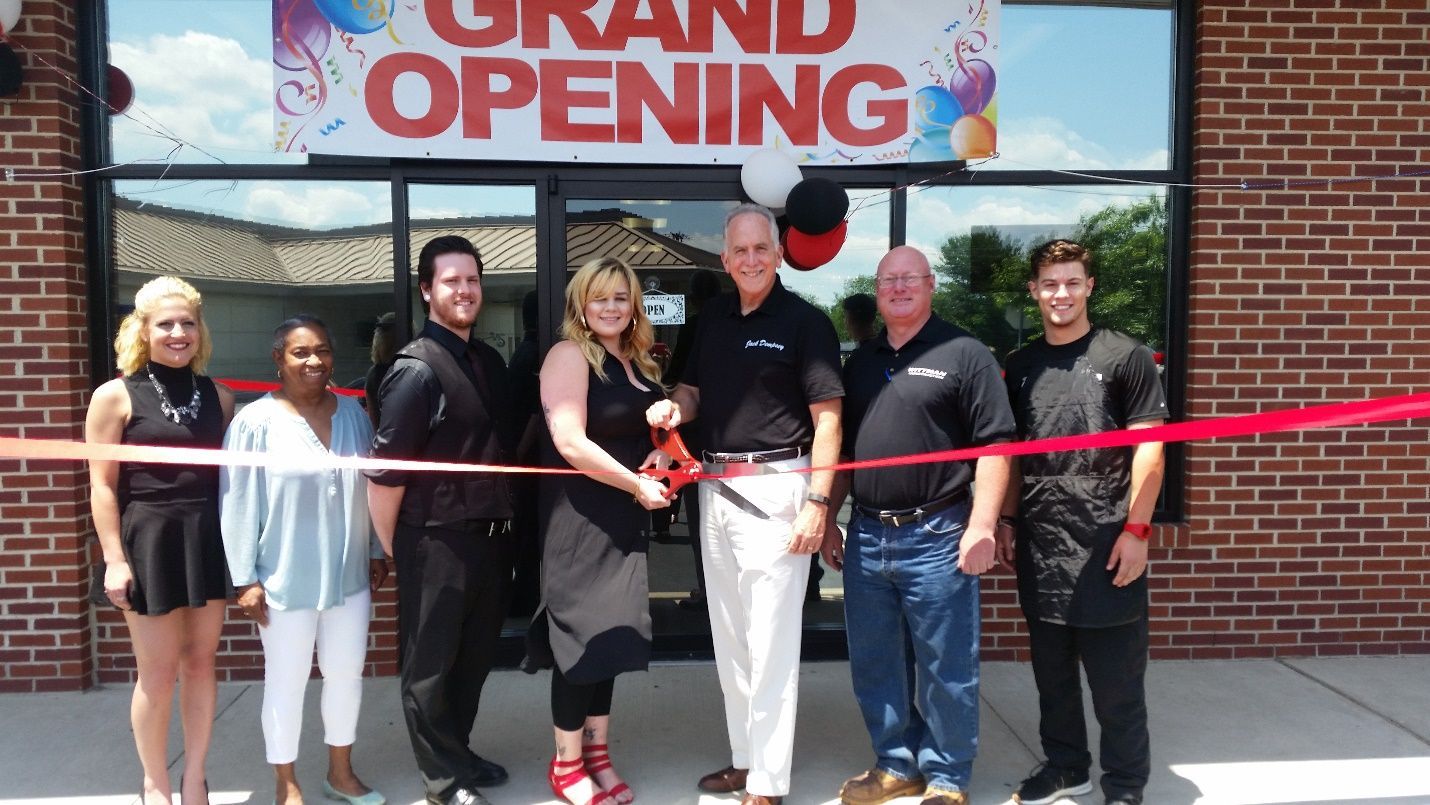 A group of people are cutting a red ribbon in front of a sign that says grand opening.