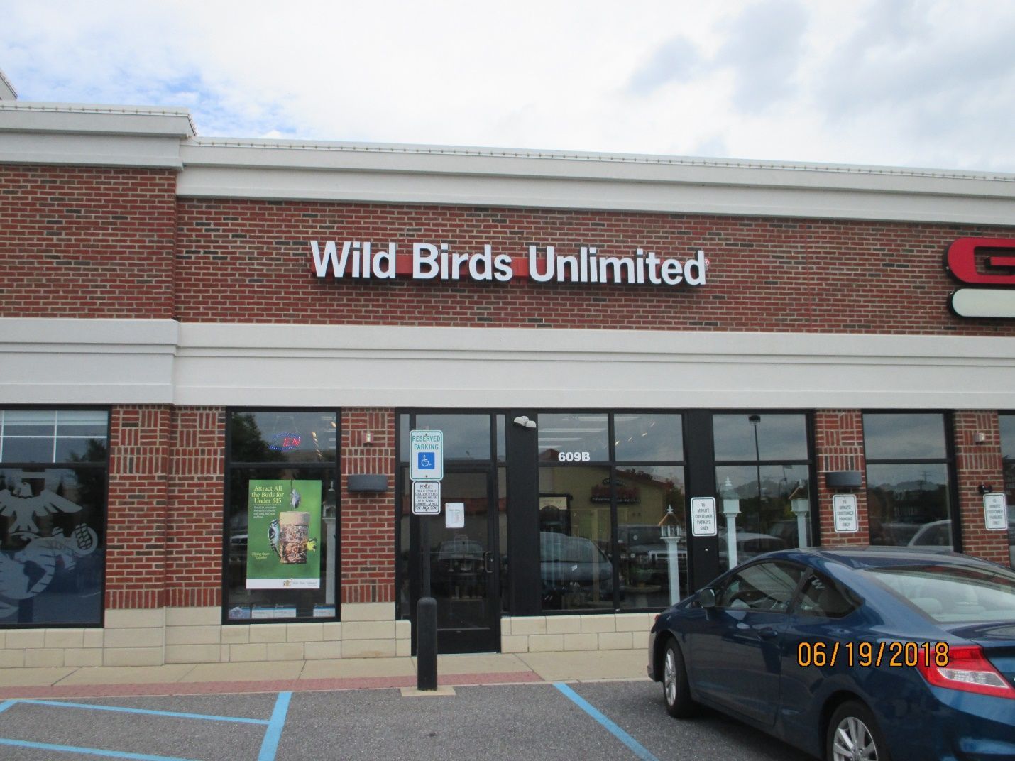 A blue car is parked in front of a wild bird unlimited store.