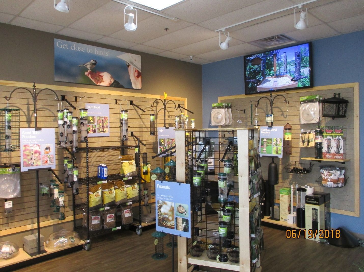 A bird feeder display in a store with a tv on the wall.