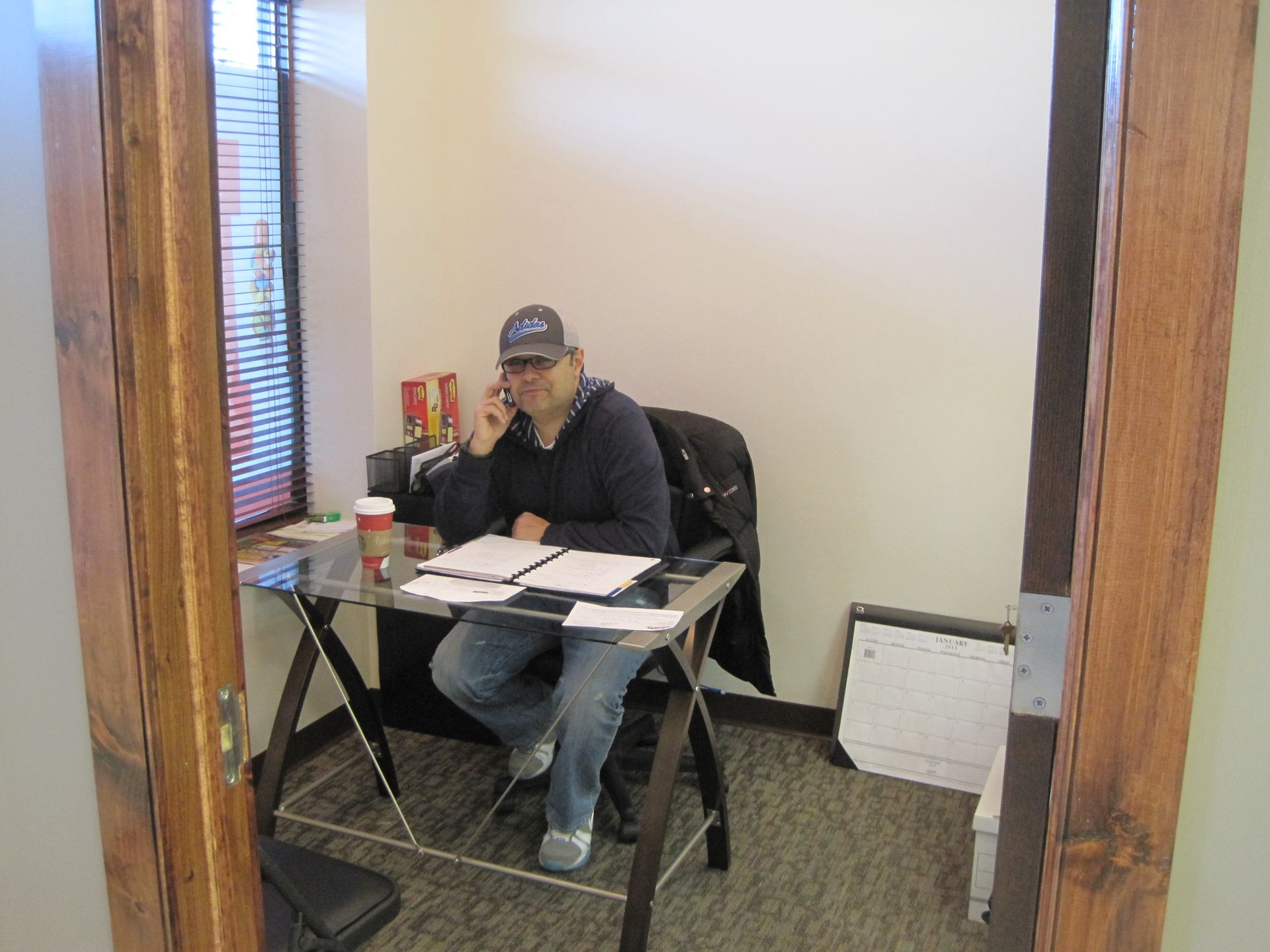 A man is sitting at a desk talking on a cell phone