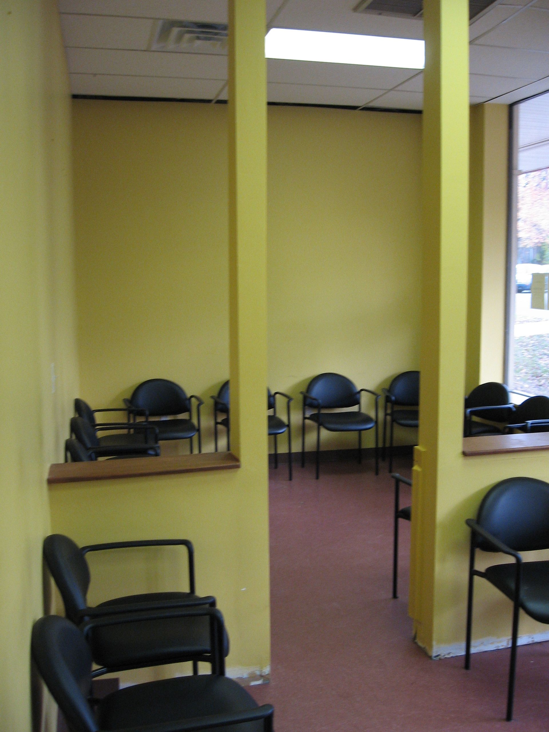 A waiting room with yellow walls and black chairs