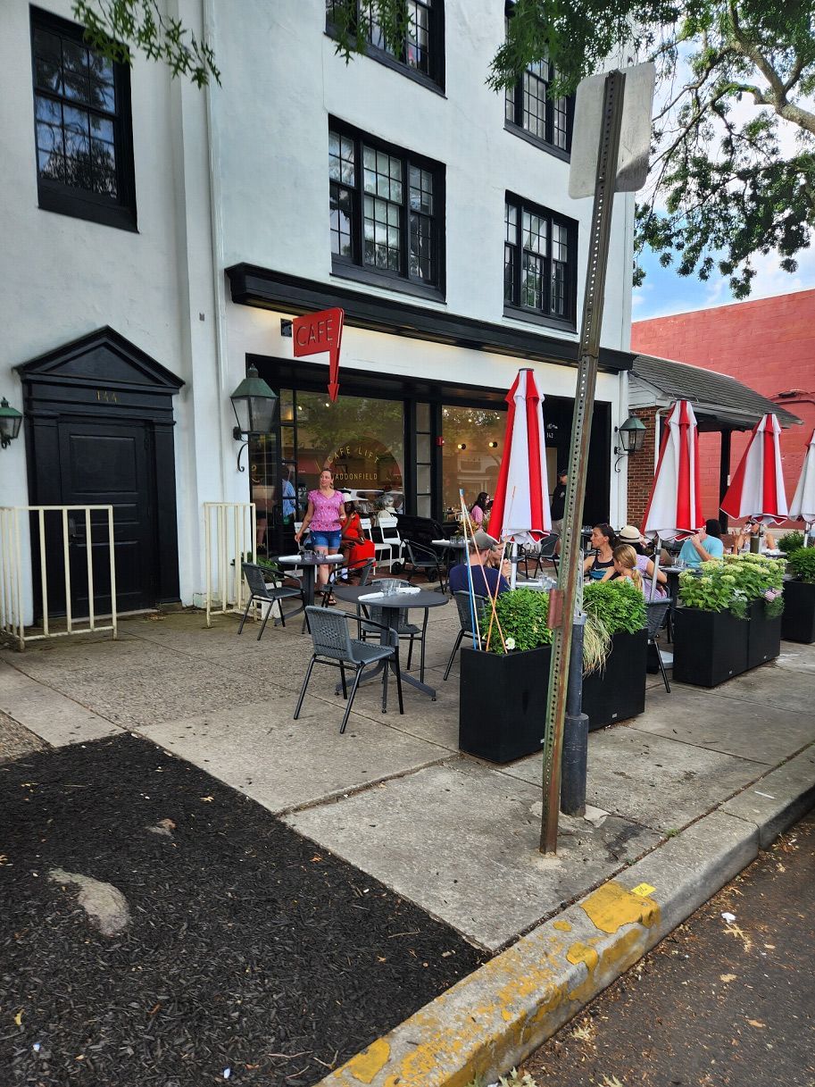A group of people are sitting outside of a restaurant with tables and umbrellas.