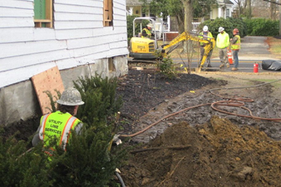 A man wearing a hard hat and safety vest is digging a hole in front of a house.
