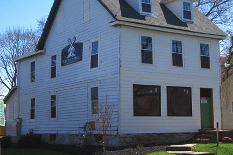 A white house with a sign on the side that says “The Barber Shop.”