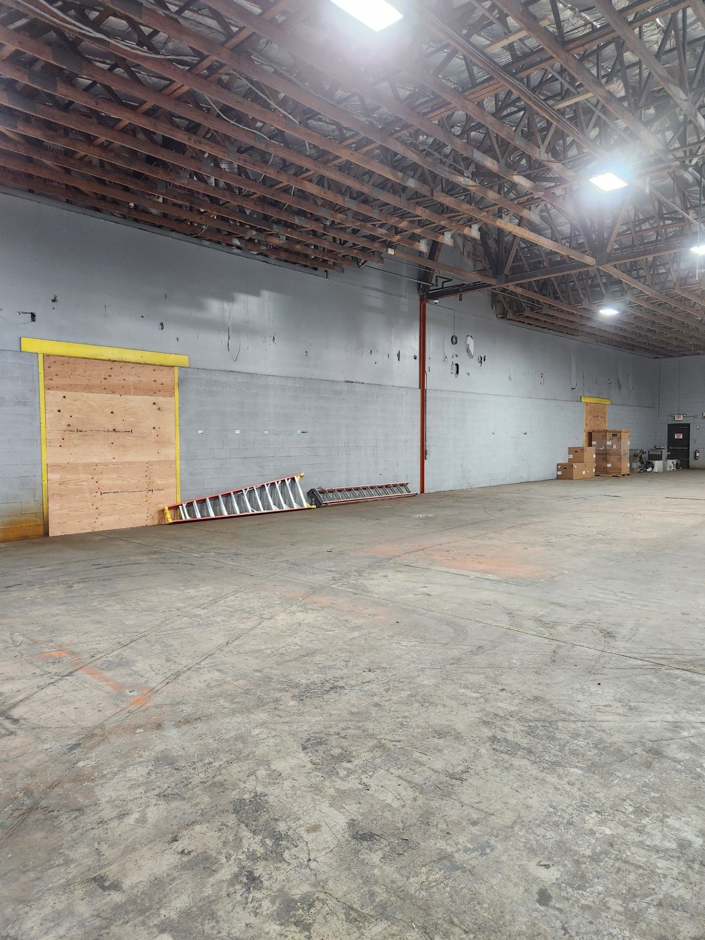 A large empty warehouse with a wooden door and a ladder.