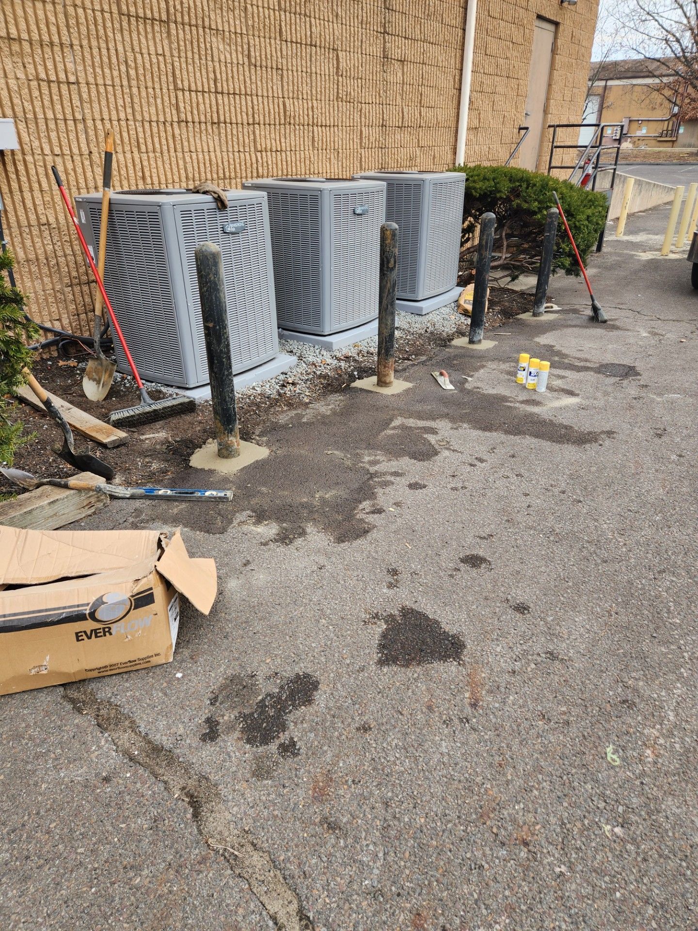 A row of air conditioners are sitting on the side of the road in front of a building.
