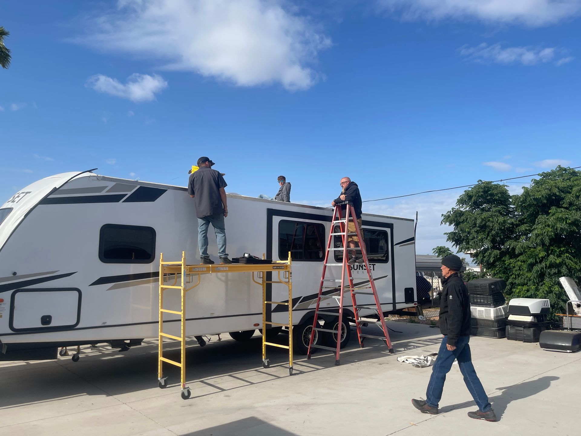 People working on the roof of a white RV under a blue sky.
