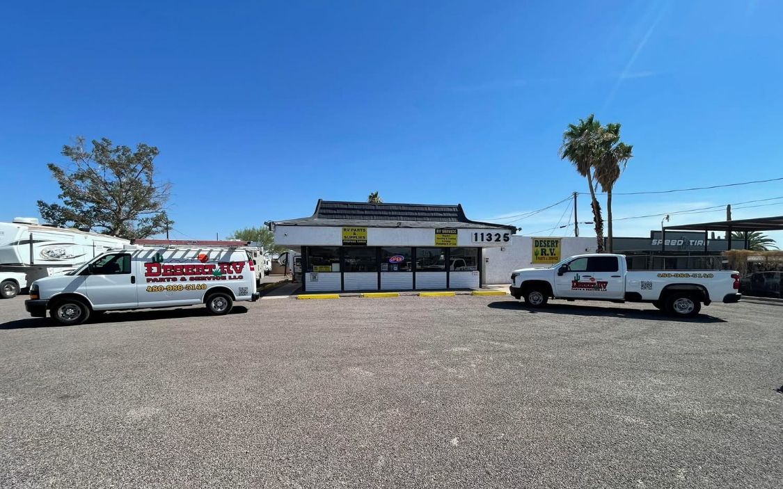 White vans and truck parked outside a small, light-colored building with a dark roof.