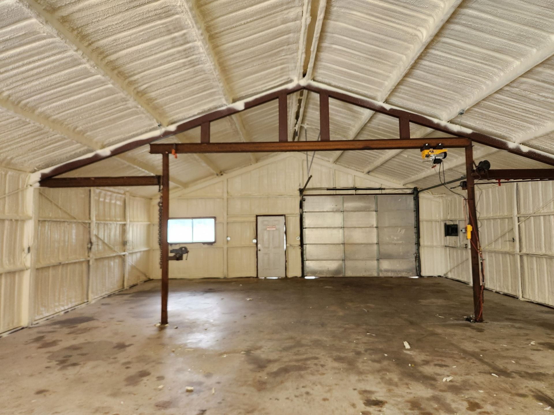 Empty warehouse interior with metal beams, corrugated walls, concrete floor, and a small window and door