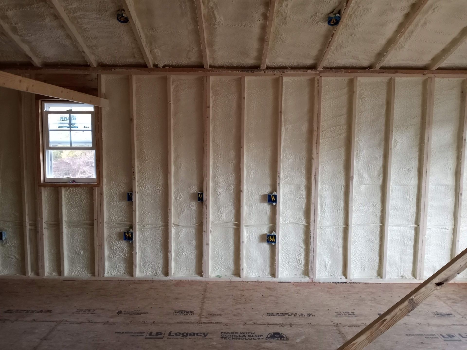 Insulated unfinished room with exposed framing, window, and plywood floor under construction