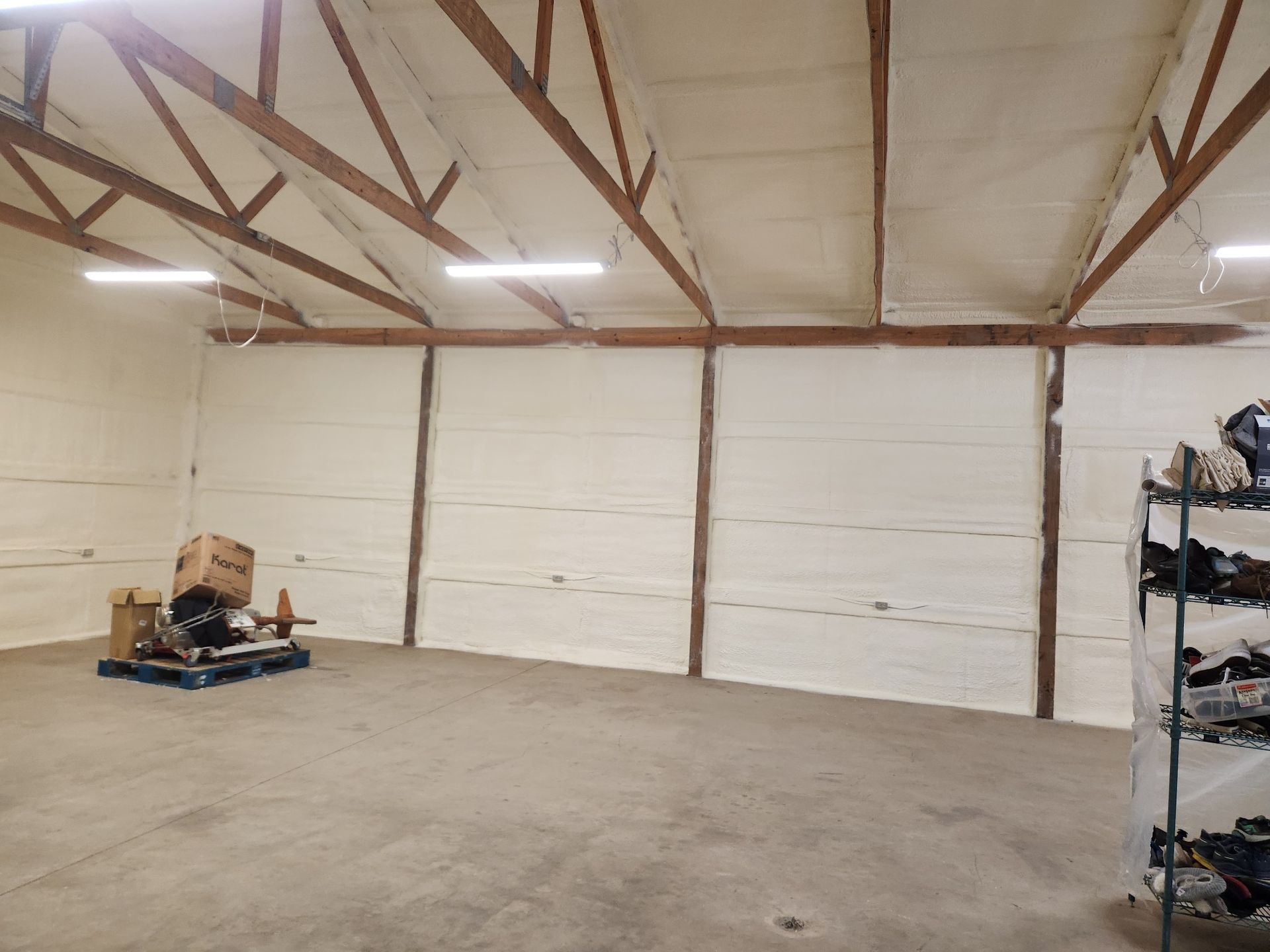Empty warehouse interior with concrete floor, white walls, exposed roof trusses, and a small cart on the left.