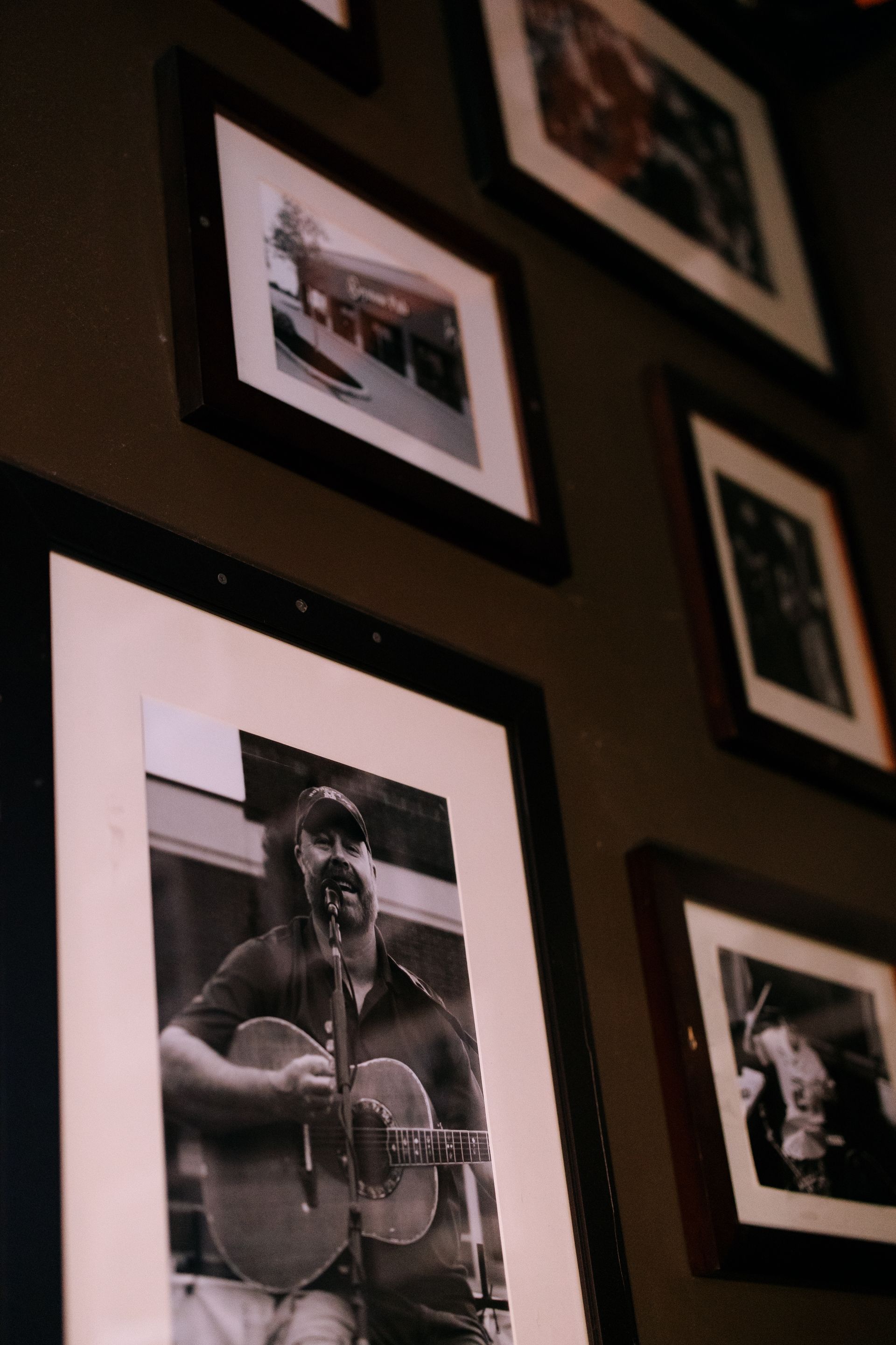 Wall with framed photos. A black and white photo of a man playing a guitar is prominent.