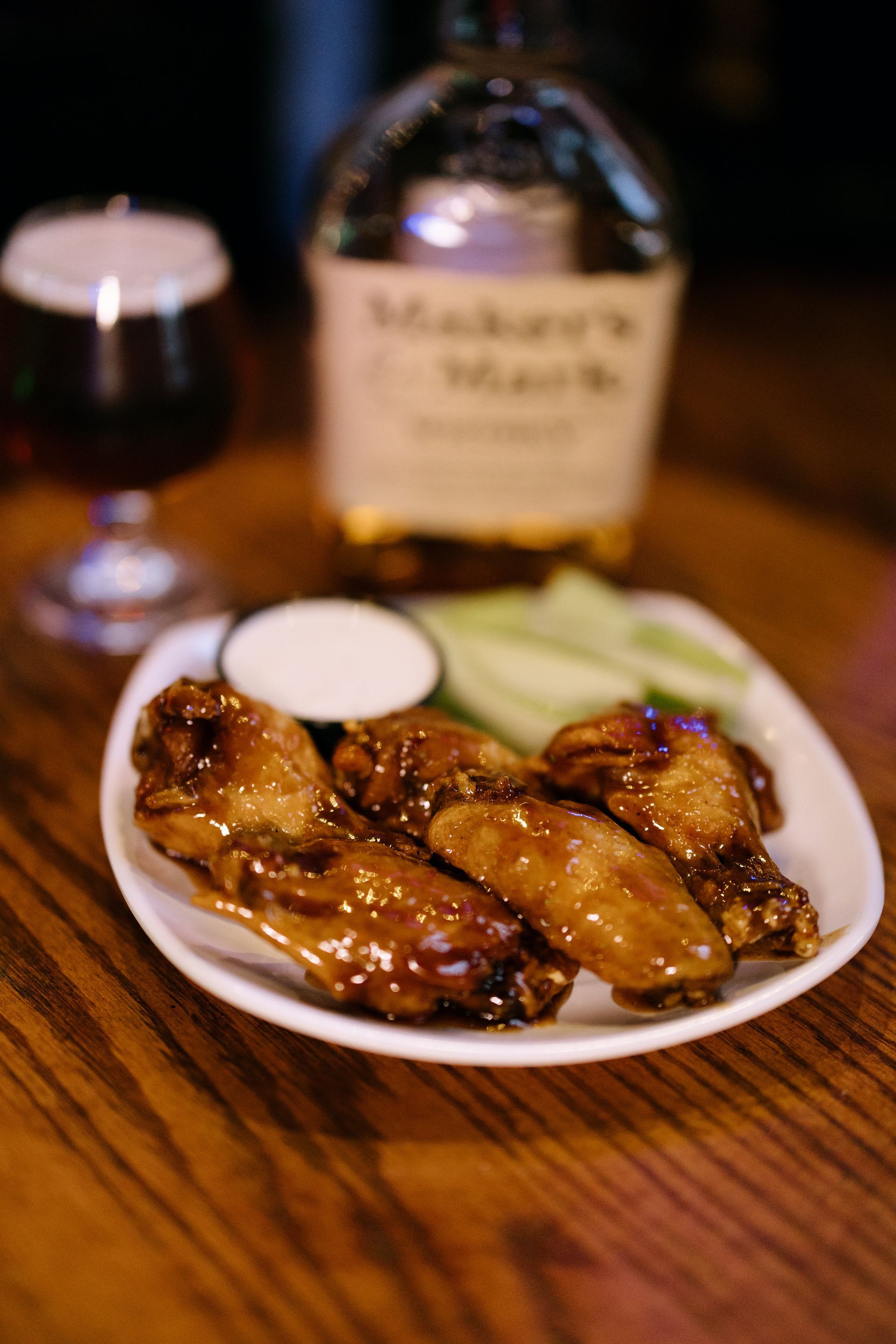 Chicken wings with dipping sauce and celery, with bourbon and beer on a wooden bar.