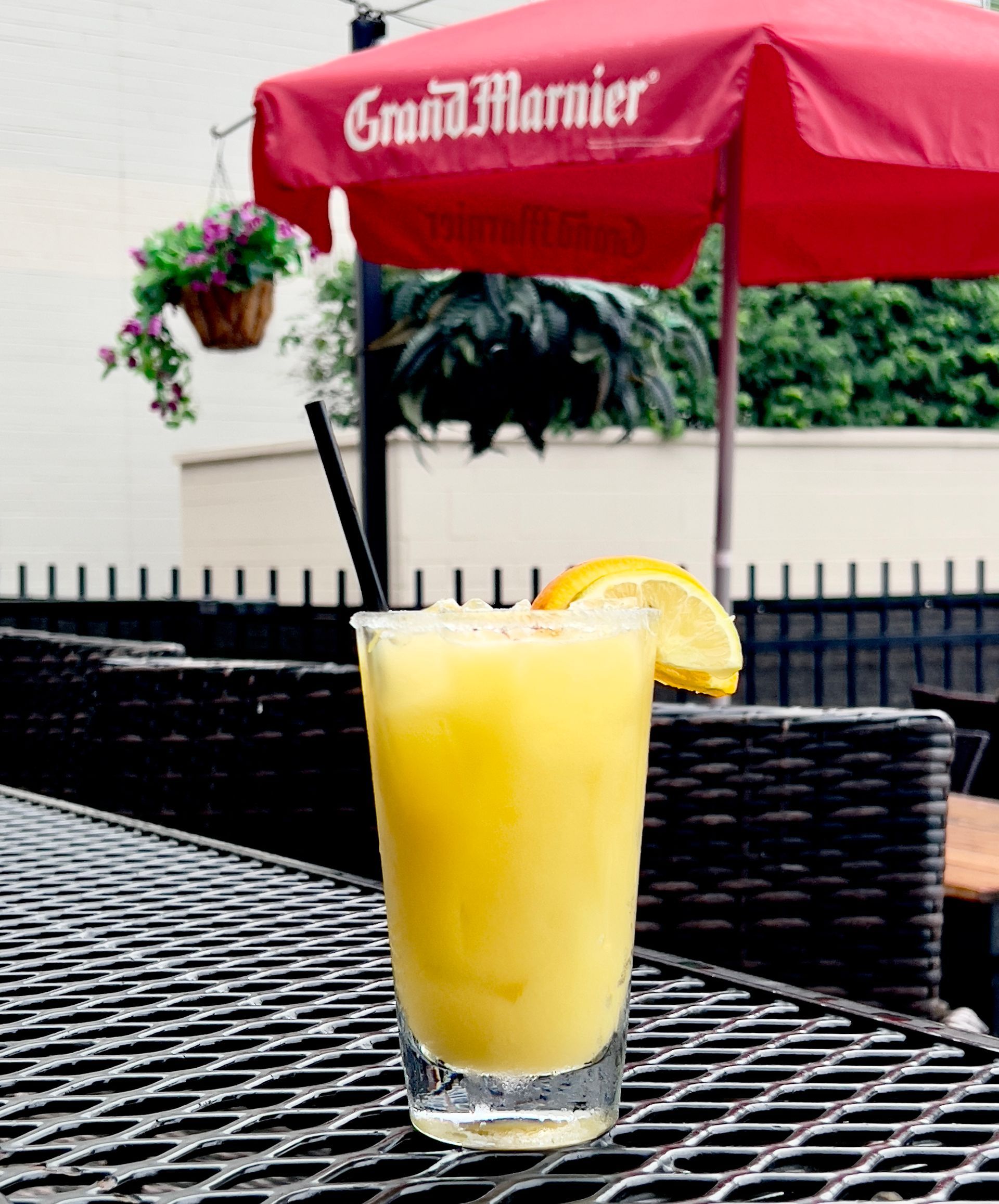 Yellow cocktail with lemon slice on a patio table under a red umbrella.