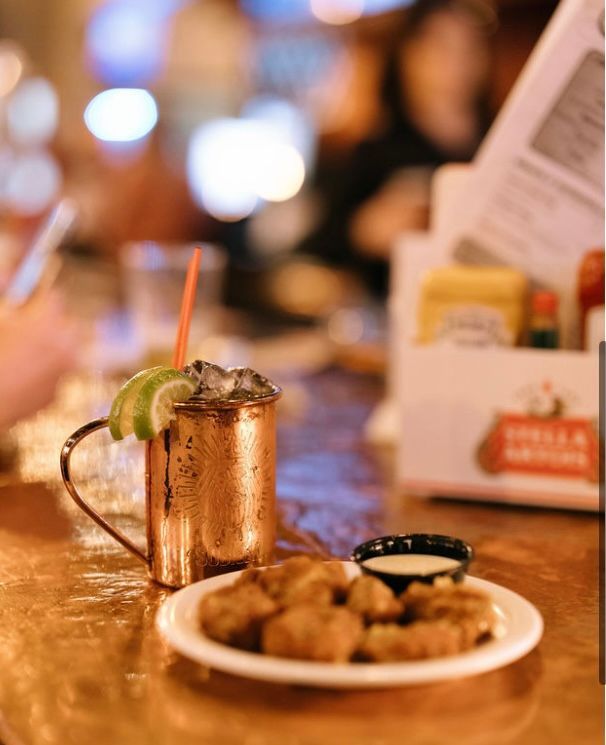 Copper mug drink and fried food on a bar. Lime garnish, copper tabletop, and a blurred restaurant background.
