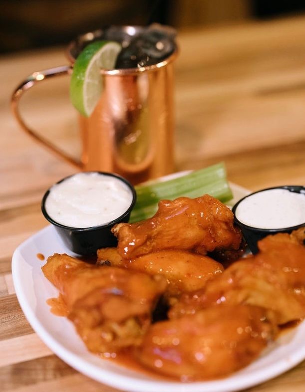Buffalo wings with dipping sauces, celery, and a copper mug cocktail with lime.