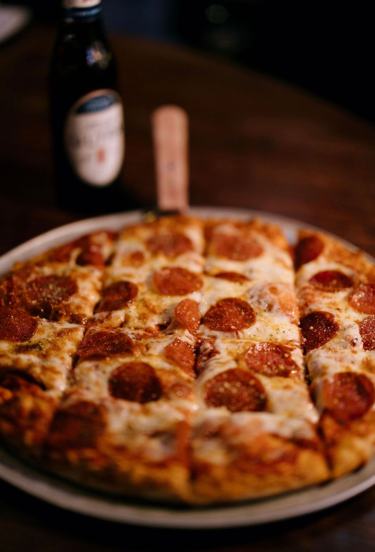 Pepperoni pizza sliced into squares on a plate, with a beer bottle in the background.