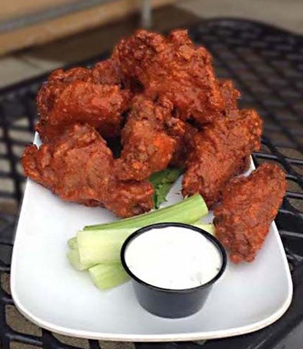 Plate of red-sauce covered buffalo wings with celery sticks and a cup of white dipping sauce on a black table.