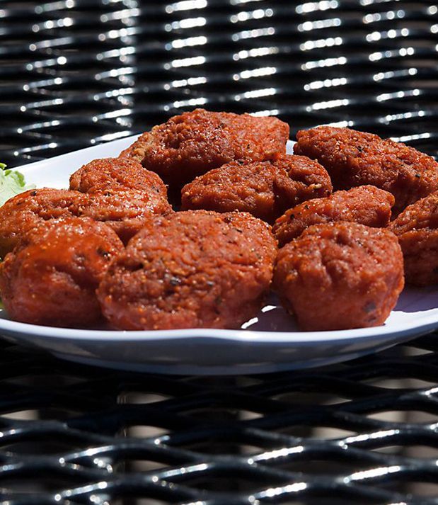 Plate of fried, reddish-brown falafel on a white plate, resting on a black metal surface.