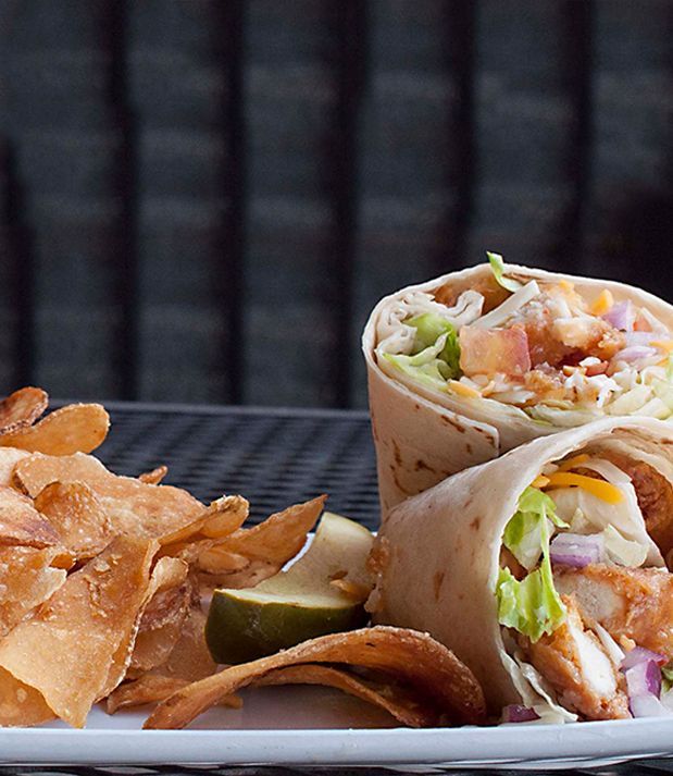 Wrap with chicken, lettuce, tomatoes, and cheese, with a side of chips and a lime wedge on a white plate.