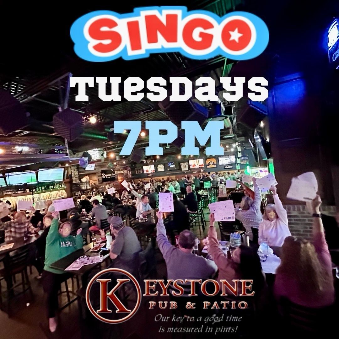 Man playing acoustic guitar on outdoor stage with string lights.