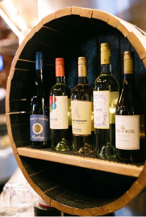 Wine bottles displayed in a wooden barrel, arranged on a shelf.