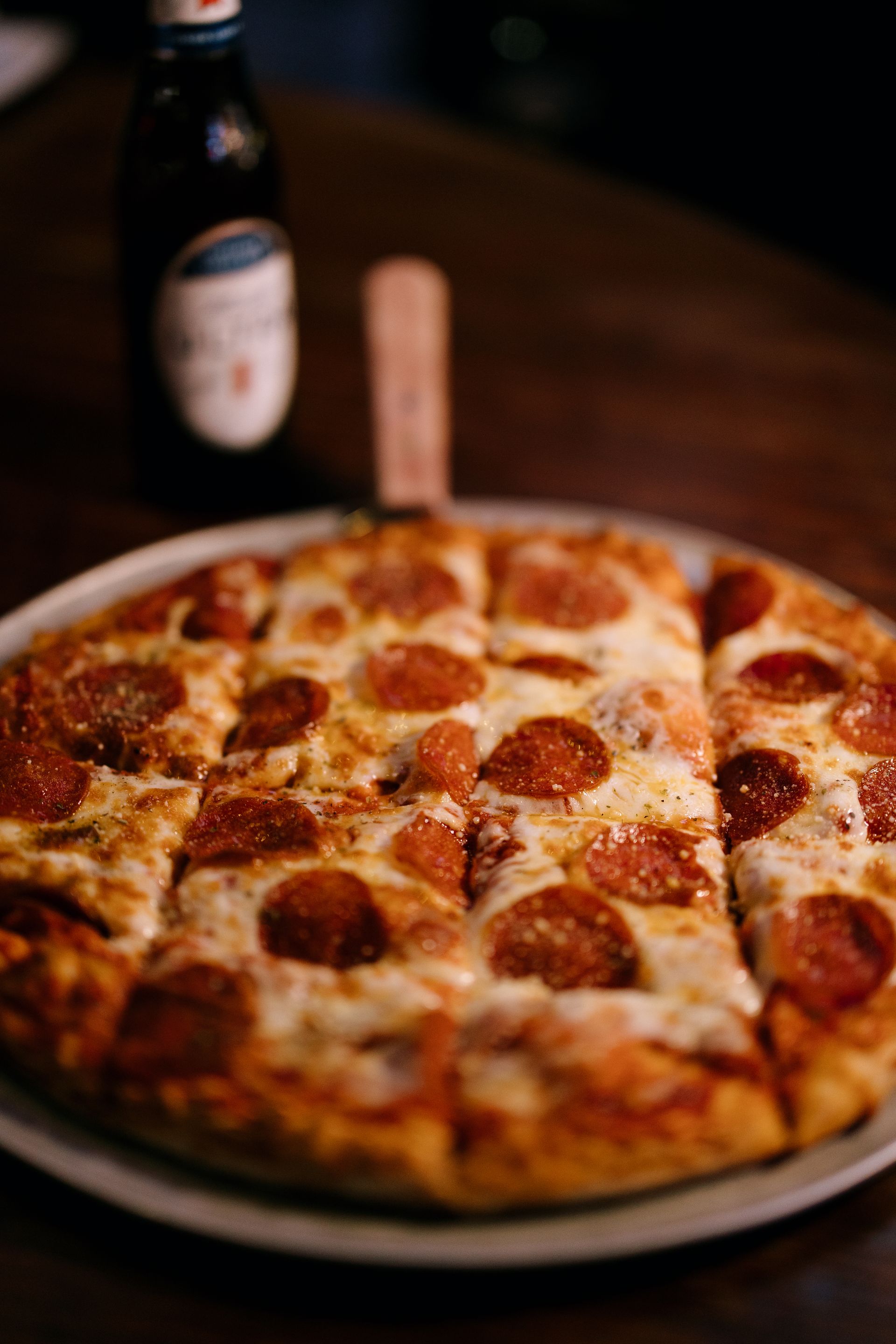 Pepperoni pizza on a plate, a bottle of beer in the background.
