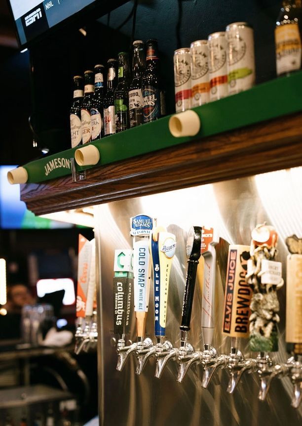 A bar with beer taps, bottles, and cans on shelves. The setting is dimly lit, with focus on the taps.