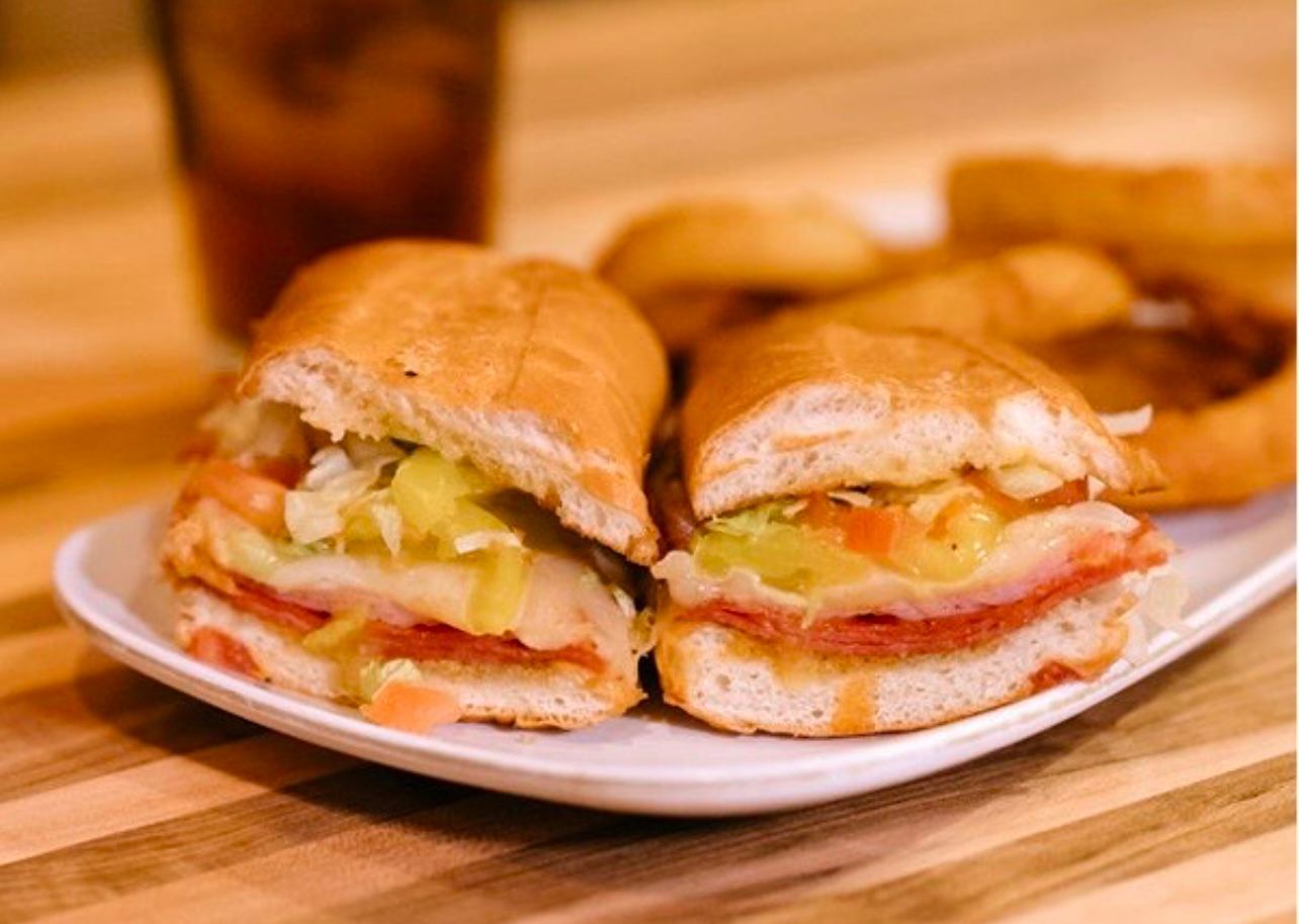 Sub sandwich cut in half on a white plate with a glass of tea in the background.