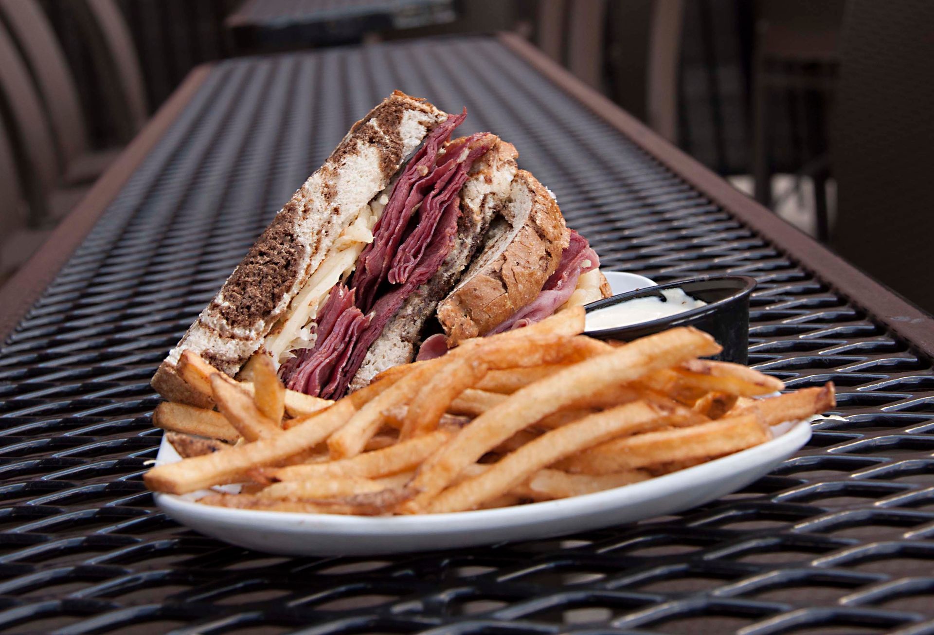 Reuben sandwich and fries on a white plate, sitting on a metal table.