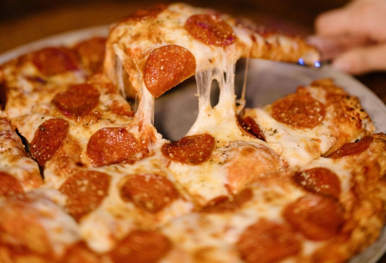 Pepperoni pizza slice being lifted, showing stretchy melted cheese.