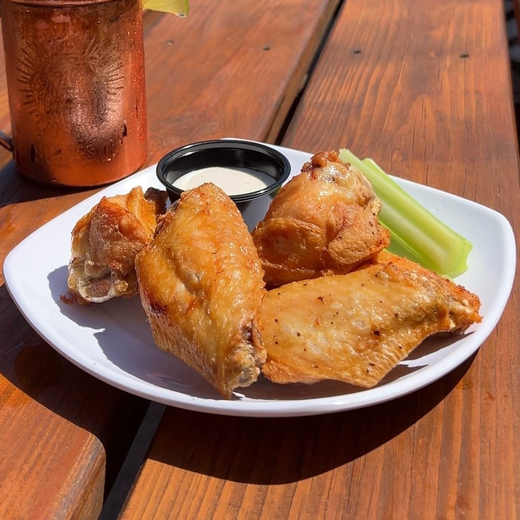Plate of fried chicken wings with ranch dip, celery, and a copper mug on a wooden table.