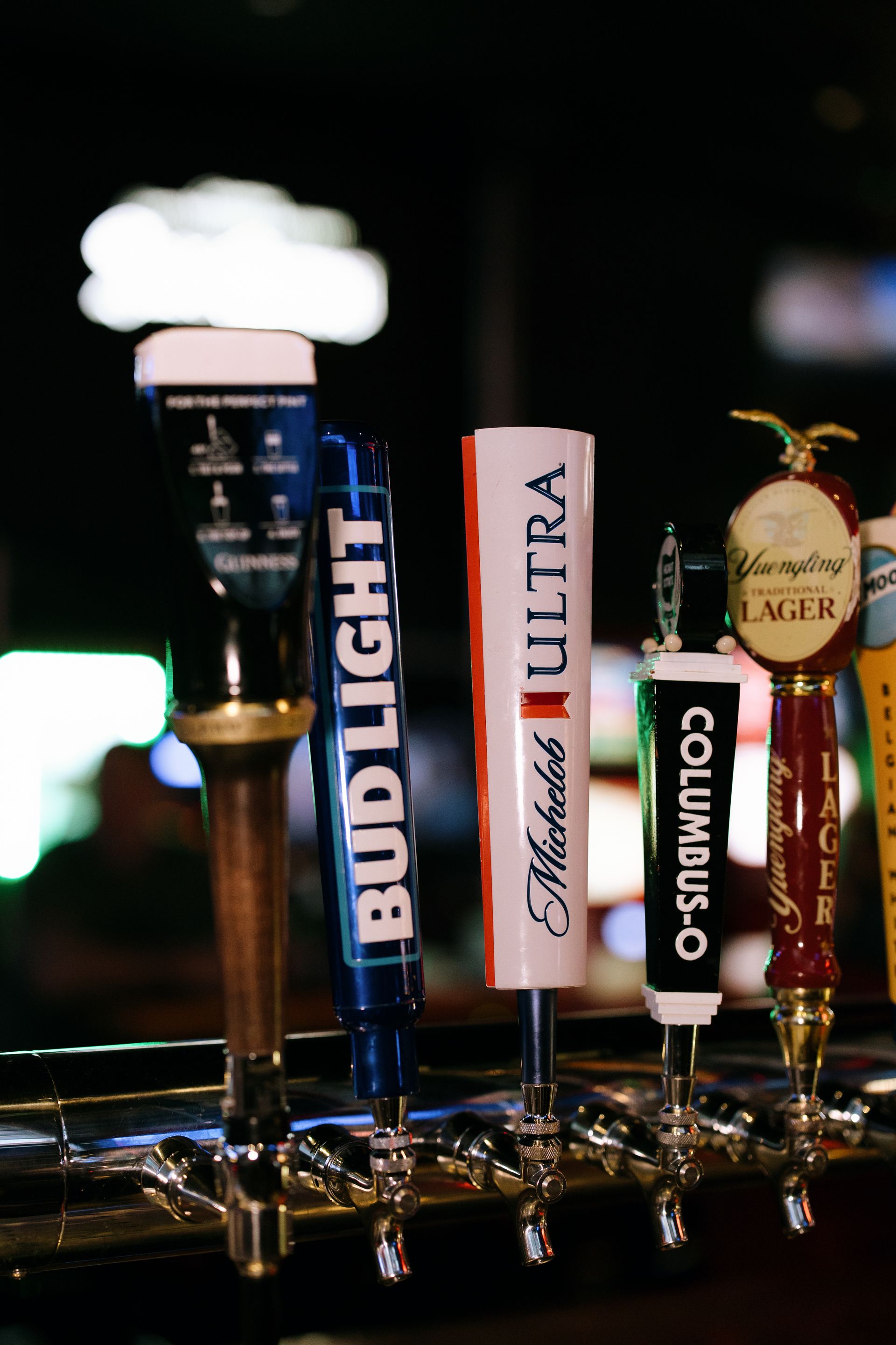 Beer taps at a bar, including Bud Light and Michelob Ultra, illuminated by a dim light.