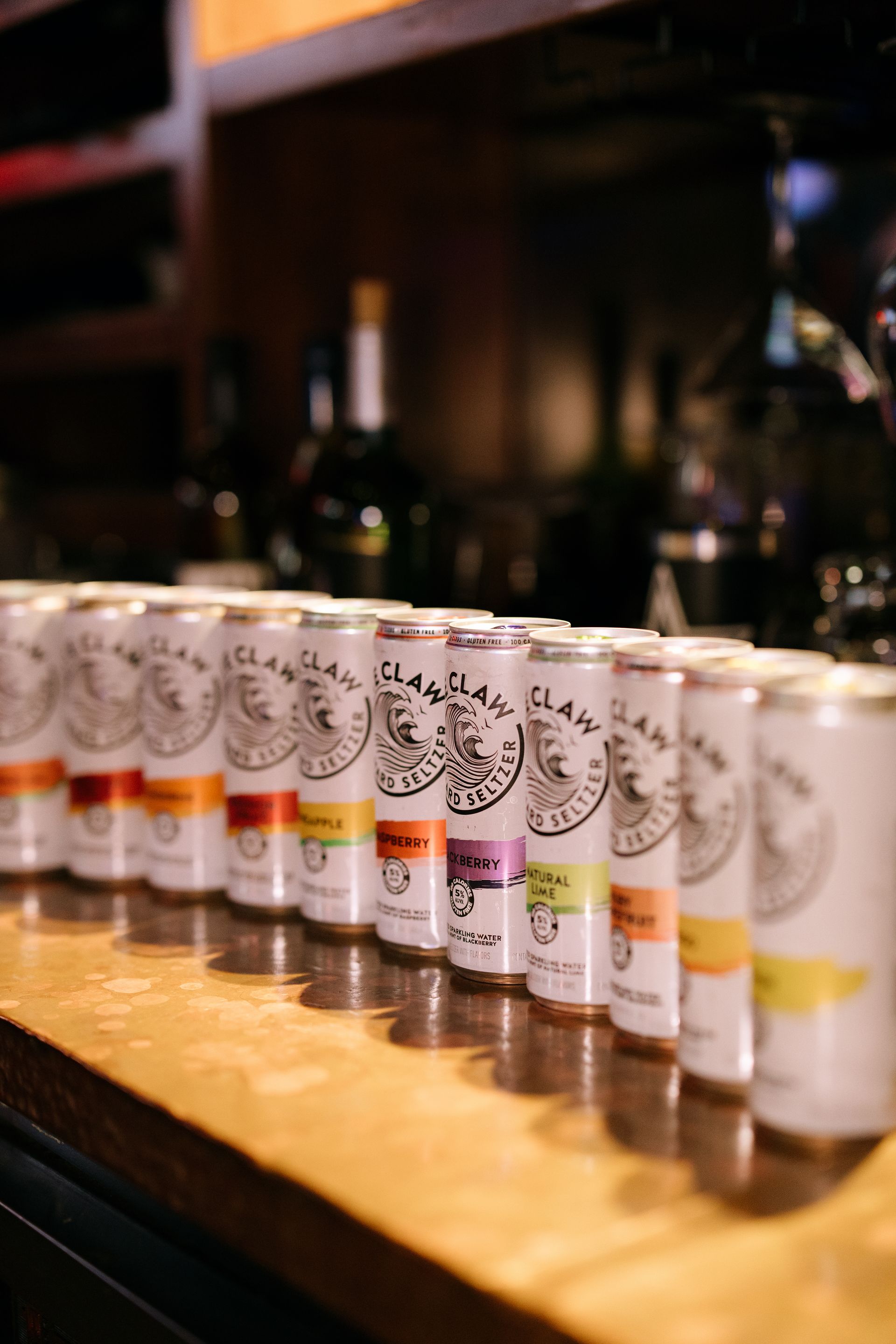 White Claw cans lined up on a bar, various fruit flavors.