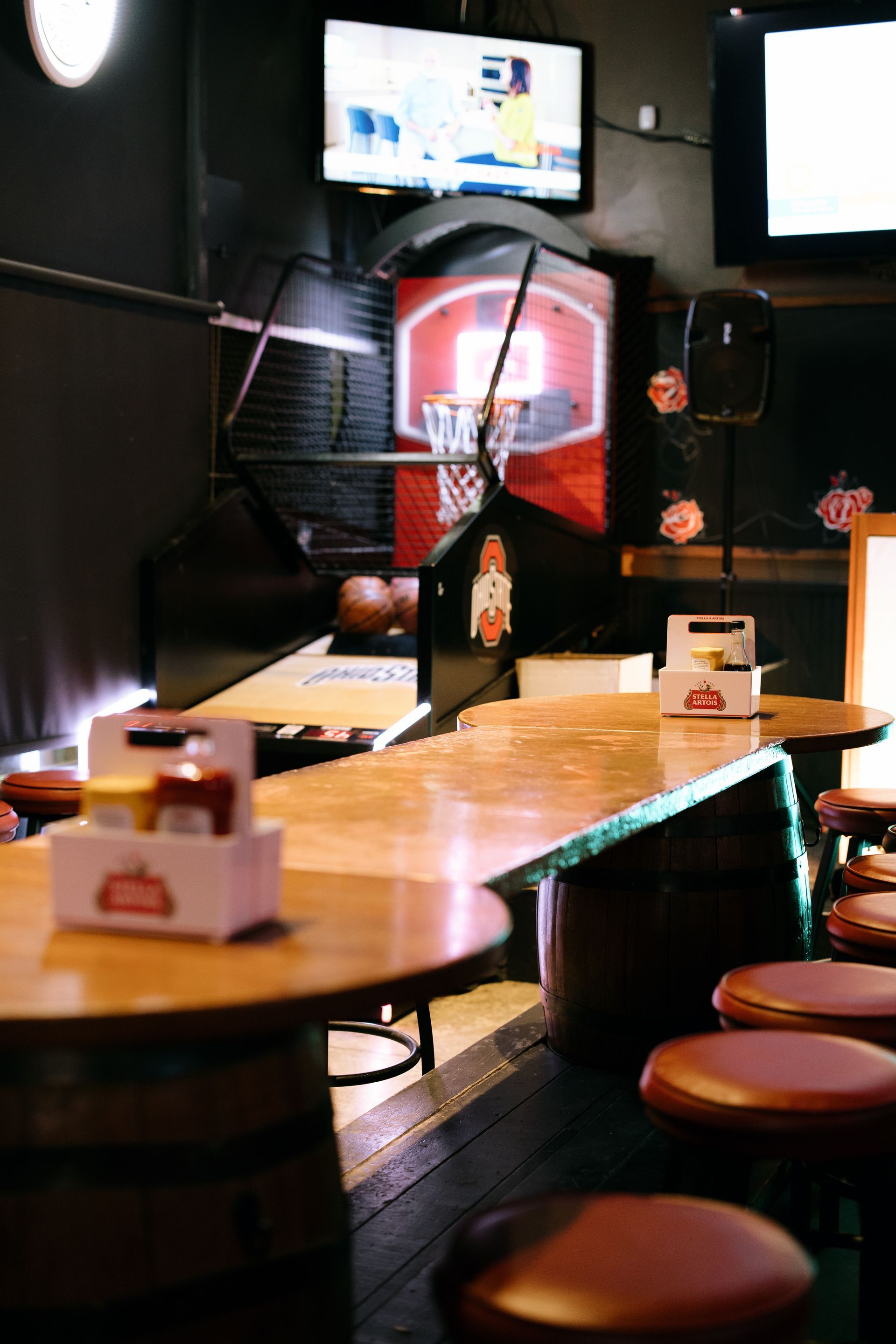 Bar interior: round tables, stools, basketball game on TV, barrel bases.