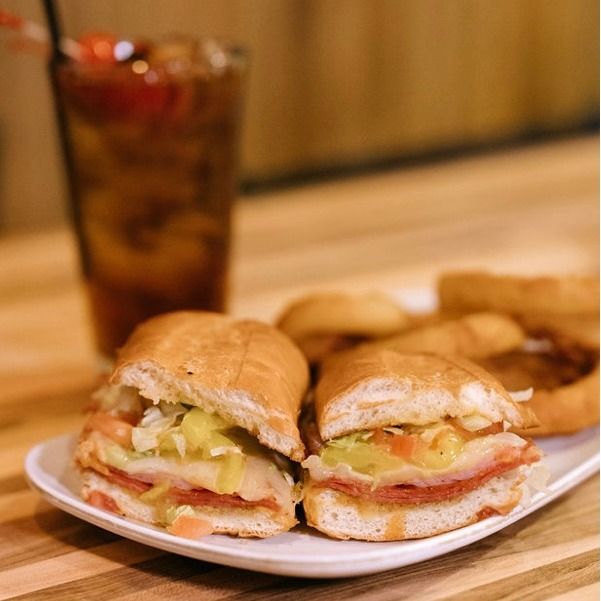 Two subs on a white plate, served with a glass of iced tea.