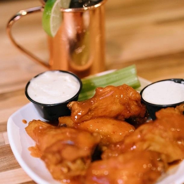 Plate of buffalo wings with dipping sauces, celery, and a cocktail in a copper mug.