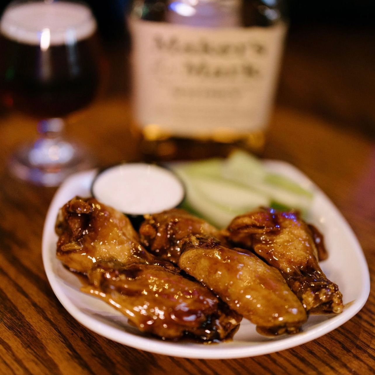 Chicken wings with dipping sauce and celery, served with a beer and bottle of Maker's Mark on a wooden table.