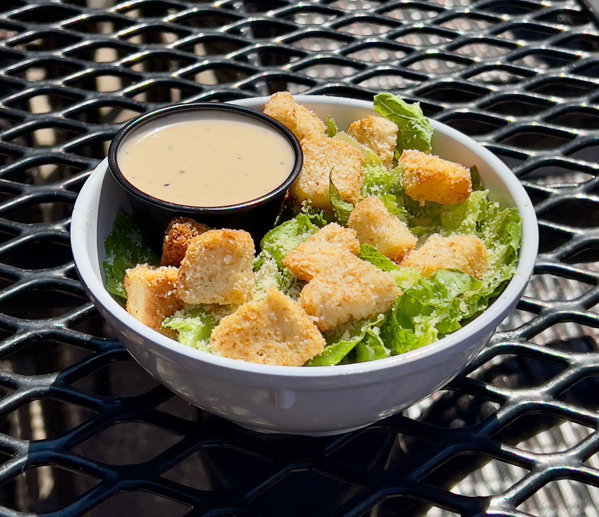 Caesar salad with grilled chicken, croutons, and Parmesan cheese in a white bowl.