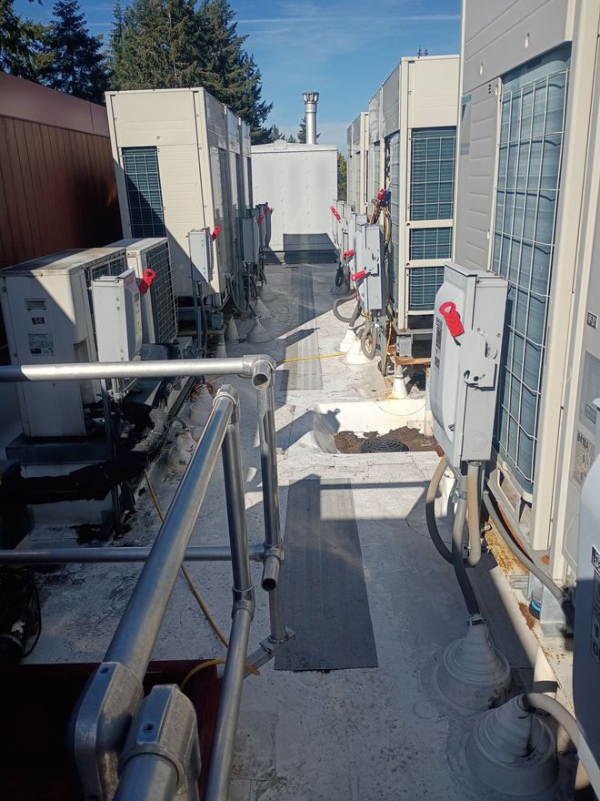 Row of outdoor HVAC units along a narrow snowy service walkway with metal railings