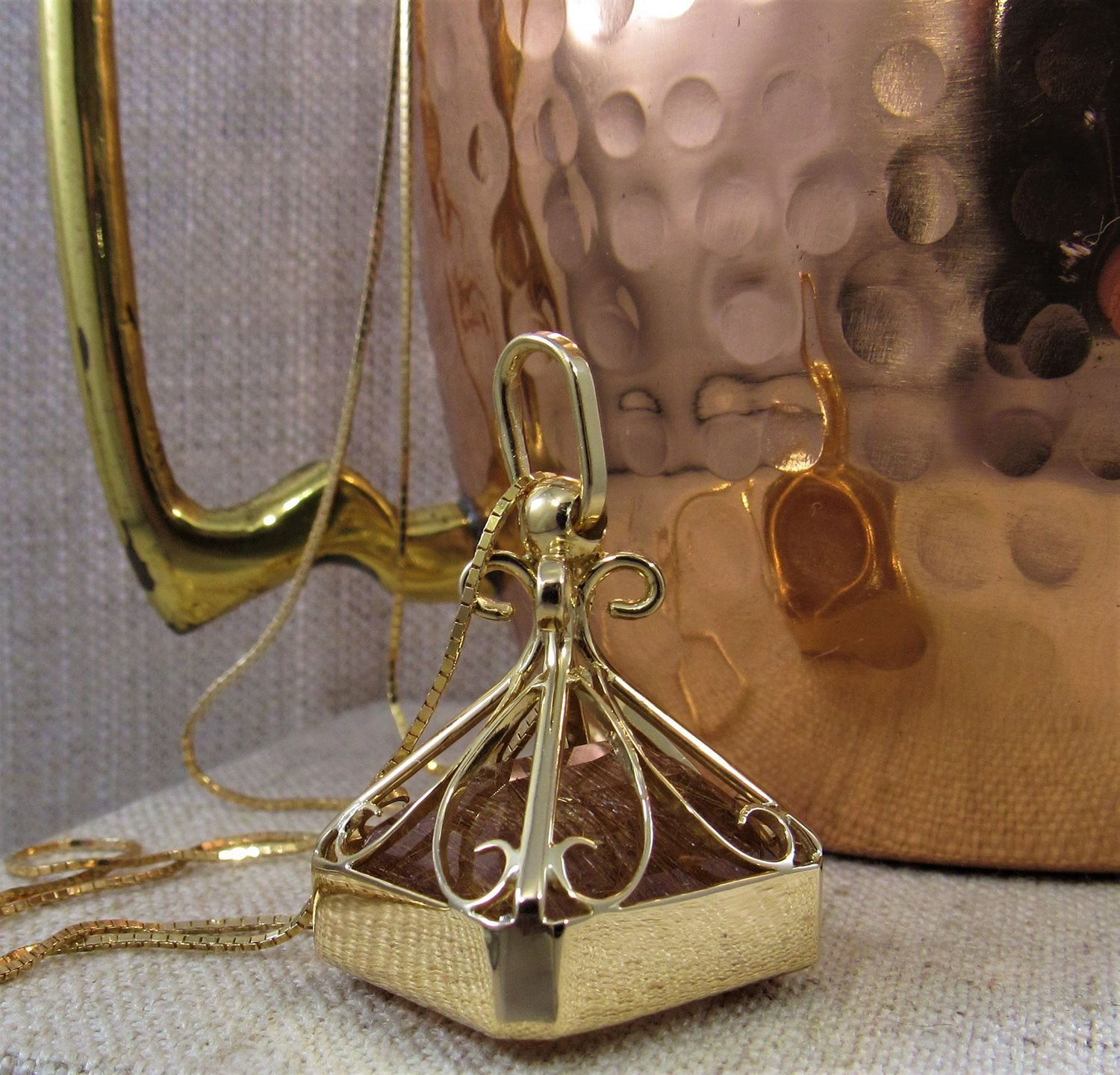 A gold necklace is sitting next to a copper pot