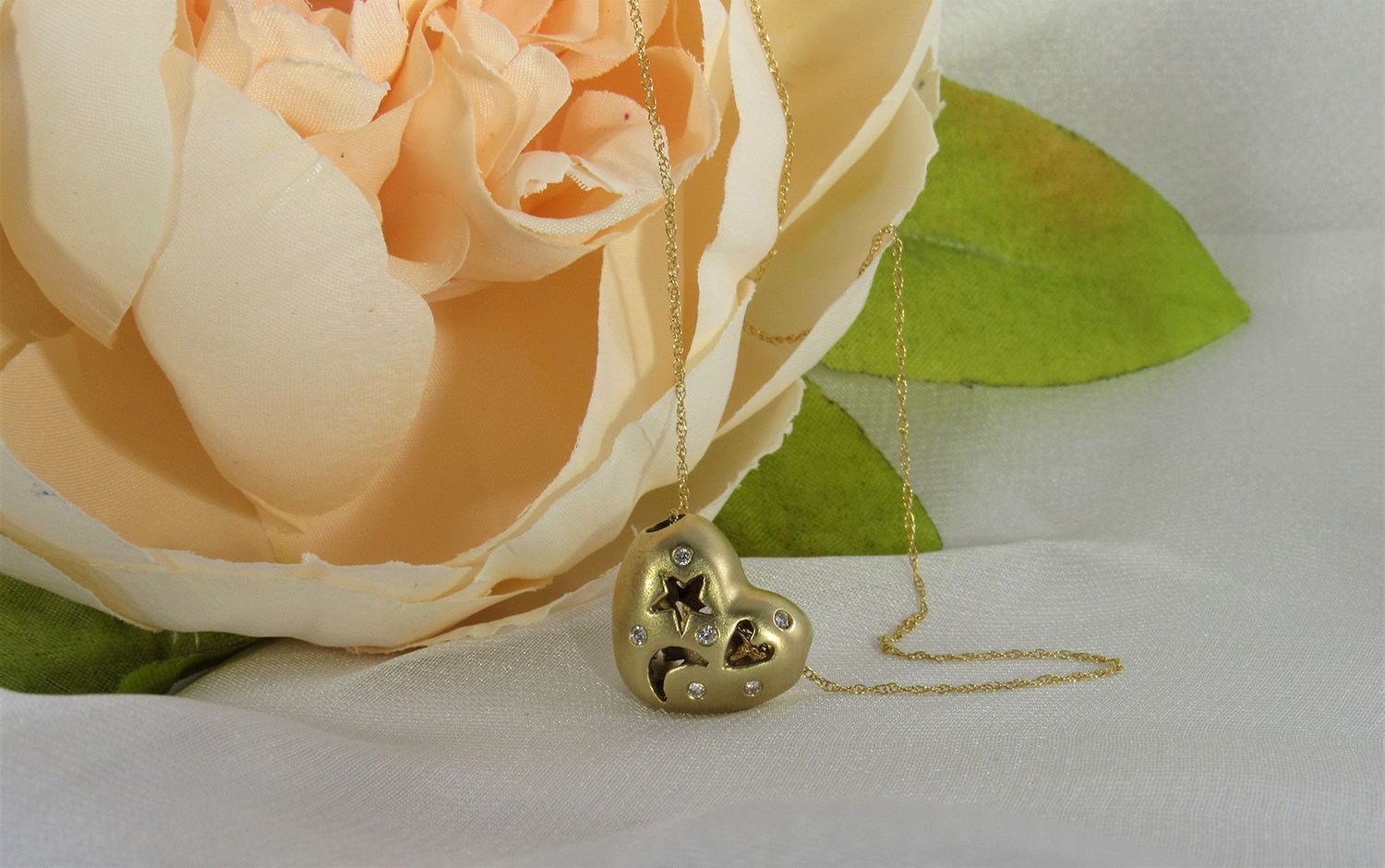 A heart shaped necklace is sitting next to a rose on a table
