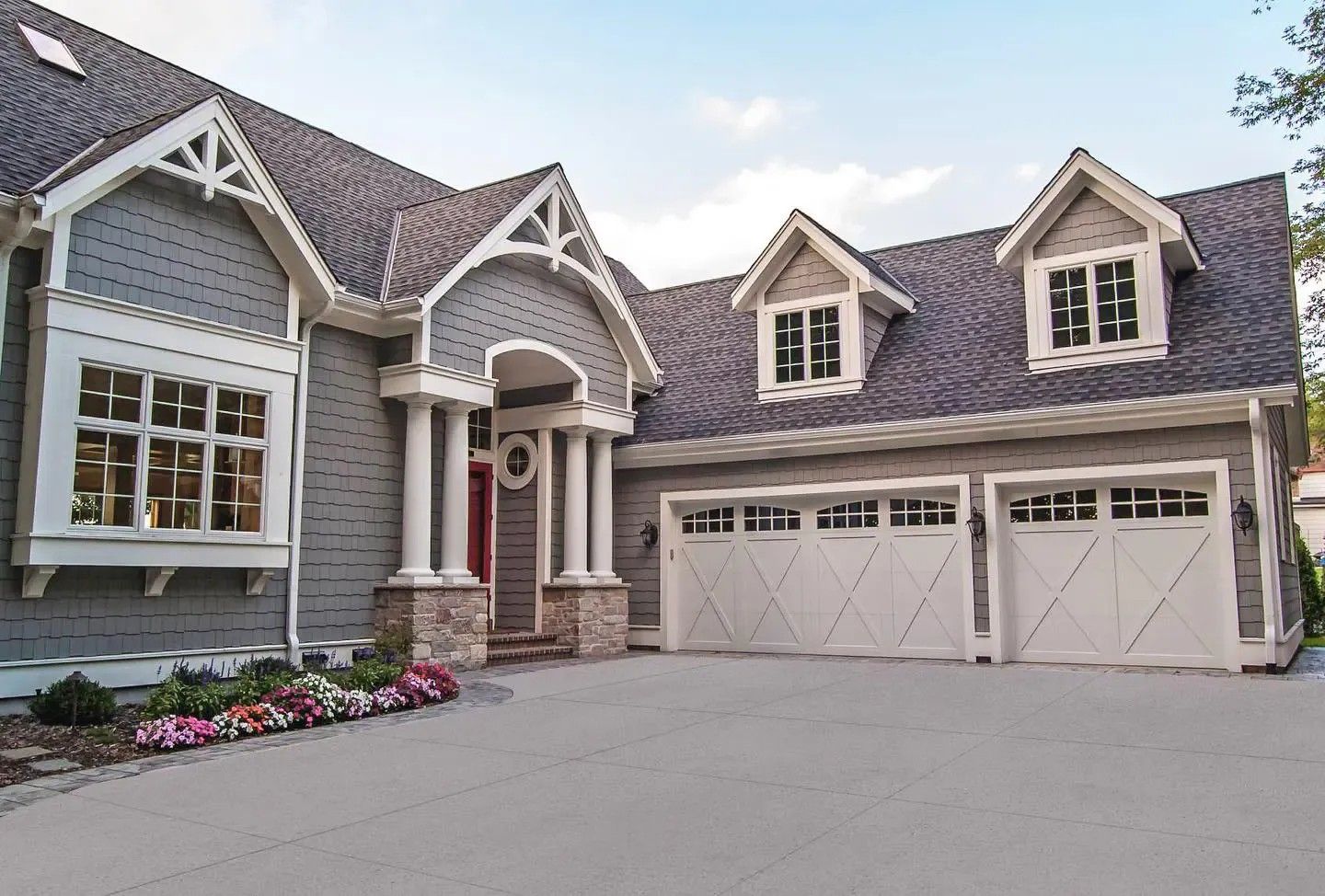 Gray house with white trim, arched entryway, and three garage doors on a sunny day.