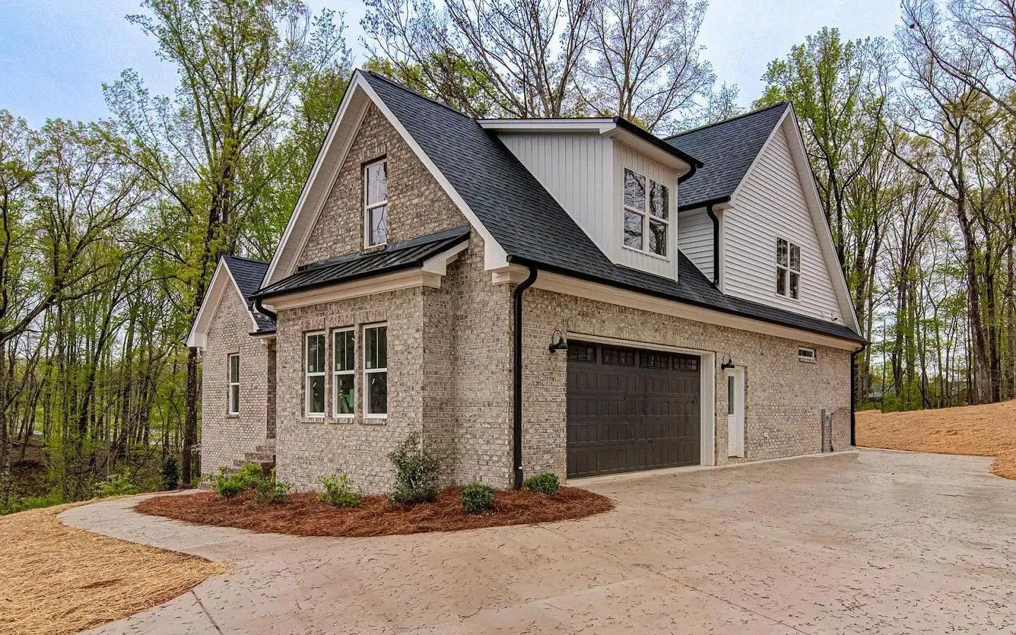 Gray brick house with black roof and garage door, surrounded by trees.