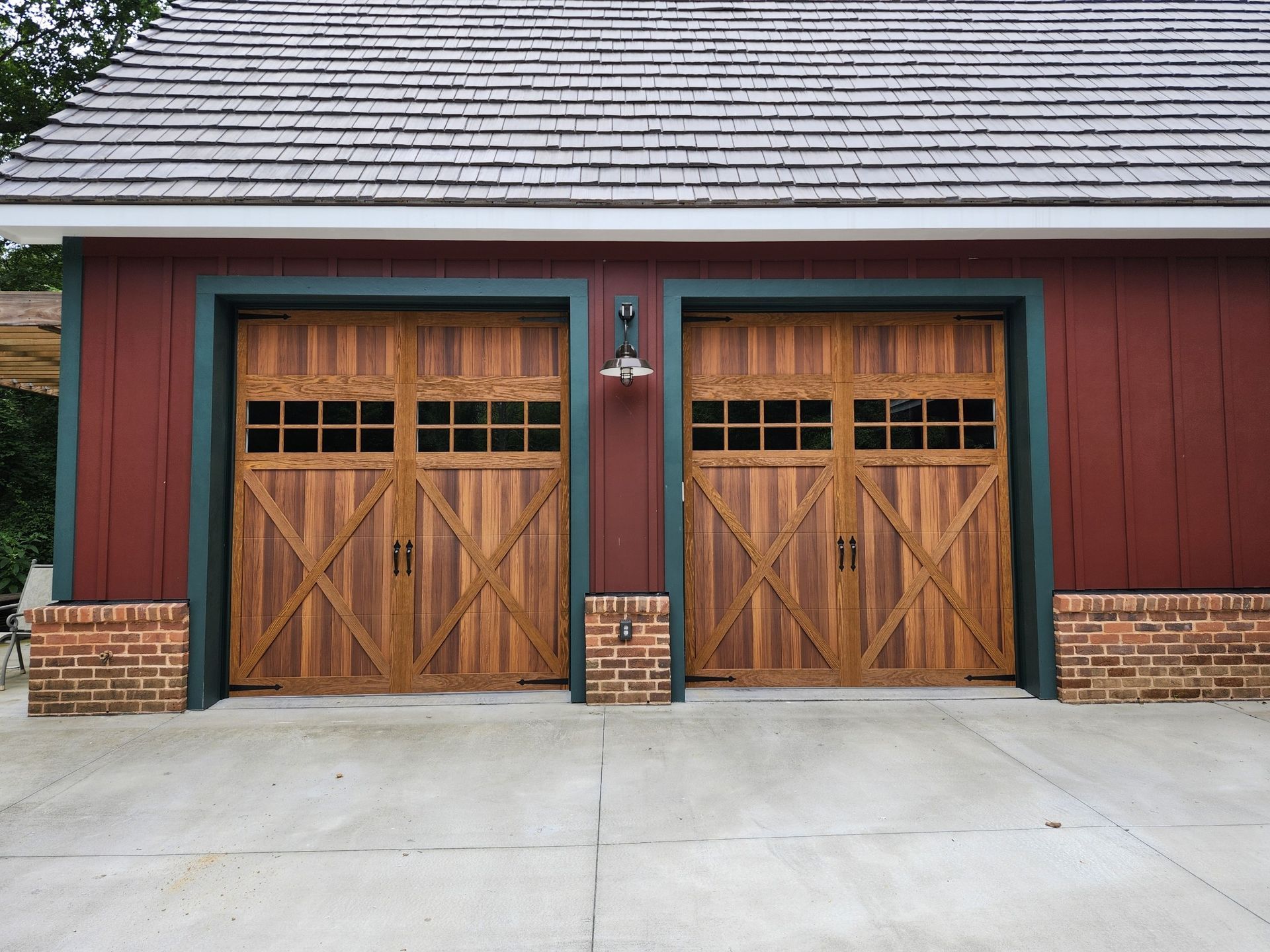Two wooden garage doors with cross design, red siding, and brick accents.